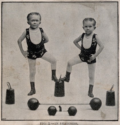 Two boys performing as strongmen. Reproduction of a photograph.