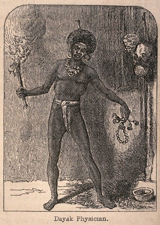 A Dayak shaman or medicine man holding a flaming torch and some charms. Wood engraving.