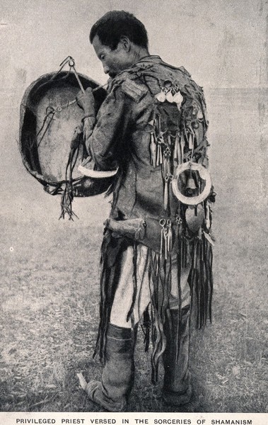 A shaman with drum and in full costume. Process print.