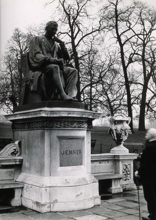 W. Calder Marshall's statue of Edward Jenner in Kensington Gardens, London; an old man standing in front of it. Photograph, 1920/1940 (?).