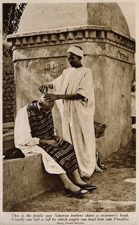 A Saharan barber shaving a man's head. Reproduction of a photograph.