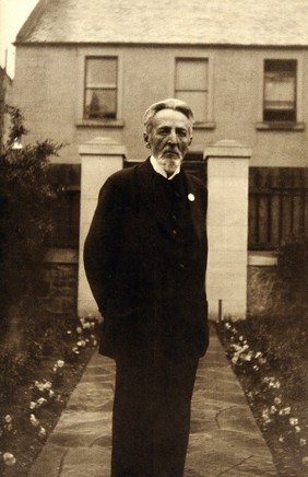 An unidentified man, standing in a garden. Photograph.