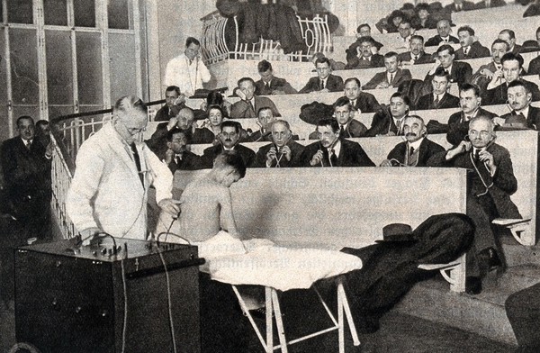 Karel Frederic Wenckebach demonstrates a boy's heartbeat to a medical class: students listen through stethoscopes connected to a machine. Process print, ca. 1925.