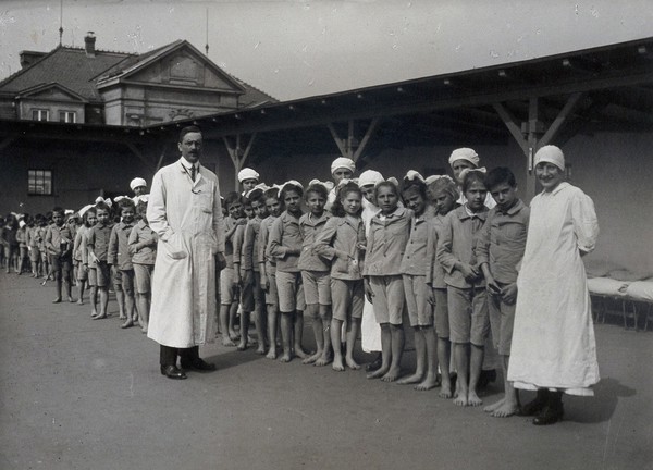 University Children's Hospital, Vienna: children and nurses in a line, fronted by the doctor in the roof garden. Photograph, 1921.