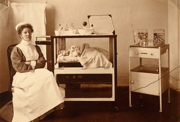 General Lying In Hospital, York Road, Lambeth: nurse sitting with baby in incubator. Photograph, 1908.