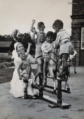 St Nicholas' and St Martin's Orthopaedic Hospital, Pyrford, Surrey: children playing on a rocking horse with a nurse attending. Photograph, c. 1935.