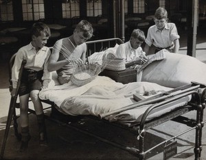 view St Nicholas' and St Martin's Orthopaedic Hospital, Pyrford, Surrey: boy patients making baskets from hospital beds outdoors. Photograph, c. 1935.