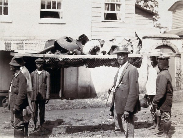 Men in Freetown, Sierra Leone, with a device for removing rubbish, which they balance on their heads. Photograph, c. 1911.