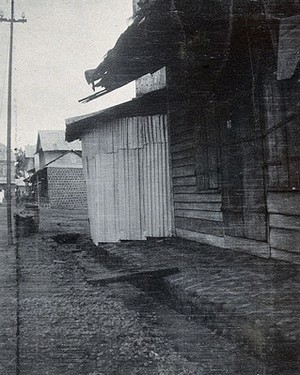 view A street in Freetown, Sierra Leone: the buildings separated from the street by a ditch, with a wooden plank to connect them. Photograph, c. 1911.