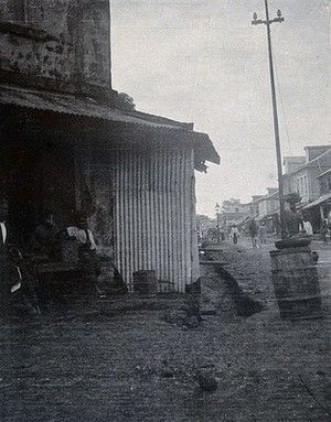 view A street in Freetown, Sierra Leone: the buildings separated from the street by a ditch, with a wooden plank to connect them. Photograph, c. 1911.