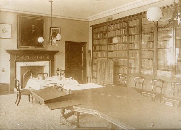 The Royal United Hospital, Bath: the library (?) with a small table laid for dining and a larger table on which rests a portable desk. Photograph, ca. 1870.