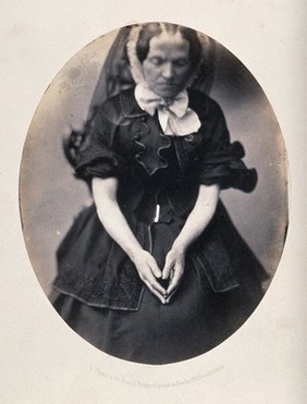 A woman, seated, wearing a black dress and veil; her hands are in her lap as though she is praying. Photograph by L. Haase after H.W. Berend, c. 1865.