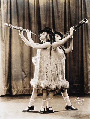 view Daisy and Violet Hilton, conjoined twins, performing with clarinets, wearing top hats. Photograph, c. 1927.