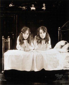 Daisy and Violet Hilton, conjoined twins, dressed for bed, kneeling to say their prayers. Photograph, c. 1927.
