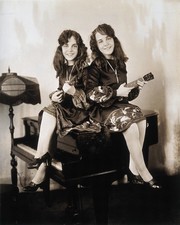 Daisy and Violet Hilton, conjoined twins, sitting on a small grand piano, holding ukeleles ...