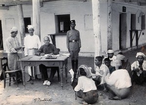 view A man sitting at a table examining passports, during a plague epidemic in Mandalay. Photograph, 1906.