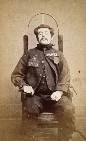 Wakefield Prison in Yorkshire: a young man with long moustaches, prisoner number 13821, his eyes are closed and he is held in a restraint-chair by his wrists and neck; head and shoulders. Photograph, c. 1869.