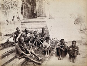 view A group of people with leprosy sitting on the steps of a pagoda in China. Photograph.