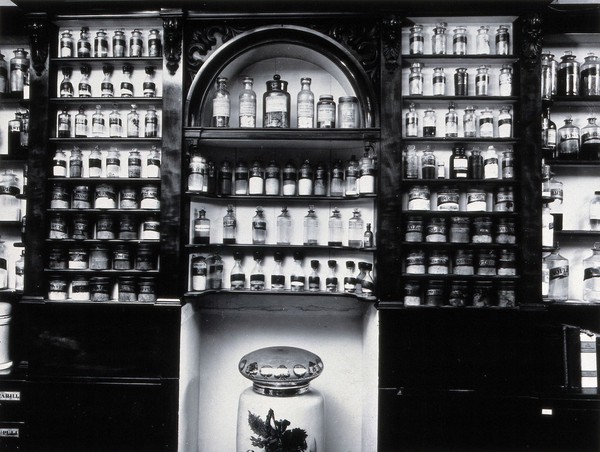 Savory & Moore Ltd, London: the interior of the pharmacy; wooden shelves with labelled bottles and jars holding drugs. Photograph.