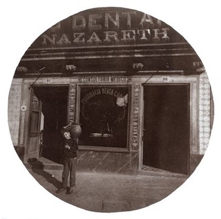 A medical surgery in Portugal; a boy carrying a jar on his shoulder is standing in the foreground. Photograph.