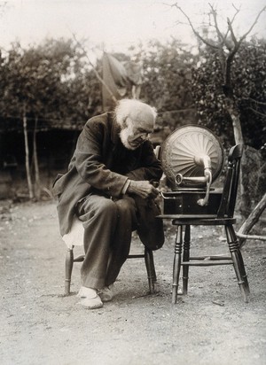 view Isaac Lamb, a centenarian, sitting on a chair outdoors, winding the handle of a gramophone. Photograph, ca 1921.