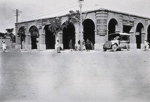 view Two men in a car outside the Wellcome pharmaceutical depot in the Middle East. Photograph.