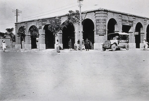 Two men in a car outside the Wellcome pharmaceutical depot in the Middle East. Photograph.