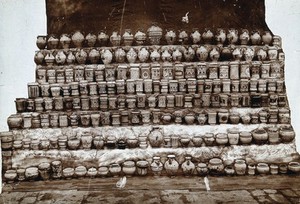 view Rows of decorated pharmacy jars and other objects. Photograph.