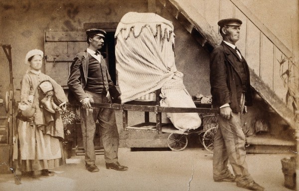 A patient covered by heavy blankets being carried away from the baths at Aix les Bains on a sedan chair by two uniformed men. Photograph.