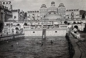 view Open air baths in Budapest: people swimming, or sitting on chairs around the edge. Photograph.
