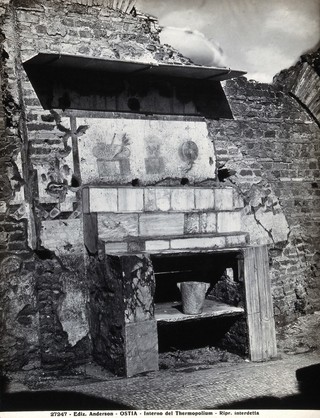 Partly ruined buildings in Ostia identified as a tavern or hot-food shop (thermopolium) from the 3rd century AD: marble steps below a fresco illustrating vegetables, wine and fruit. Photograph by Anderson.