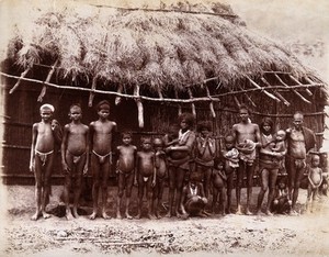 view A group of adults and children standing in a line outside a bamboo hut with a thatched roof: Bombay at the time of the plague. Photograph, 1896/1897.