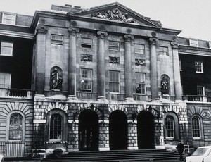 view The front entrance of Guy's Hospital, with statues of Aesculapius and Hygieia above the arches. Photograph.