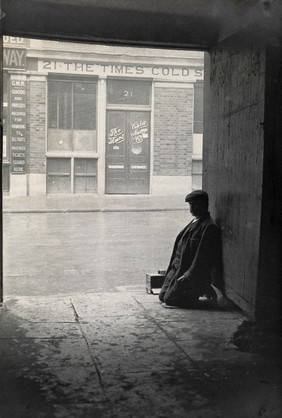 The church of St. Bartholomew the Great and surrounding area; a man kneeling in a passageway. Photograph by G.W. Miller, 28 November 1909.