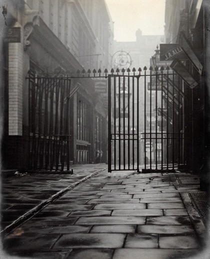The church of St. Bartholomew the Great and surrounding area; iron gates leading to Westmorland Buildings, looking west. Photograph by G.W. Miller, 28 November 1909.