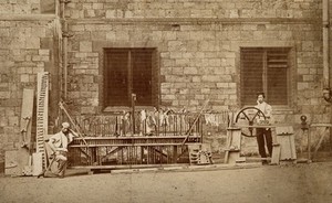 view Two men standing next to a complex wooden apparatus. Process print.