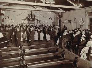 view Metropolitan Lunatic Asylum, Kew, Victoria (Australia): patients, mostly children, entertaining some seated adults in a small wooden hall. Photograph.