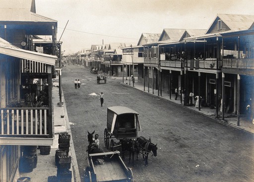 Colón, Panama: tarmacadamed street with storm sewer; residents shown in houses and on the street, with horse and cart in the foreground. Photograph, 1911.