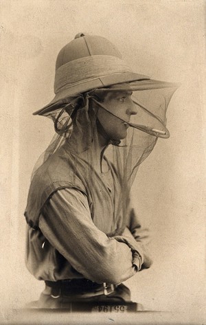 view Mosquito headnet worn with a hat, modelled by a man in profile smoking a cigarette. Photograph, 1902/1918 (?).