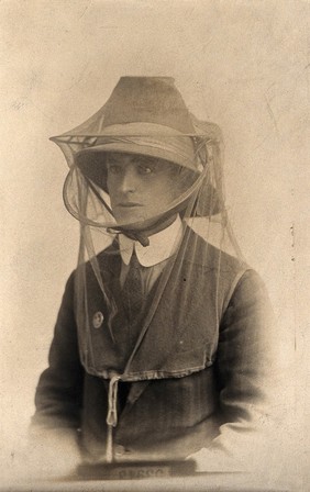 Mosquito headnet worn over a hat, modelled by a man wearing a collar, jacket and tie. Photograph, 1902/1918 (?).