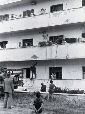 Malaria control equipment, Italy: hoses are looped up inside an apartment building; view of balconies with residents in doorways. Photograph, 1940/1950 (?).