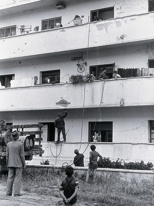 view Malaria control equipment, Italy: hoses are looped up inside an apartment building; view of balconies with residents in doorways. Photograph, 1940/1950 (?).