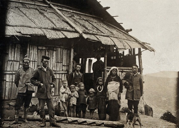 Indian (cinchona plantation?) workers: men, women and children in front of a hut, Bengal, India (?). Photograph, 1910/1920 (?).