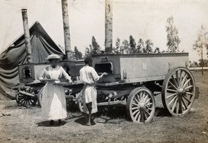 view Mobile ovens for food provision to the King's African Rifles (KAR), Nairobi, Kenya; a Western woman and an African man unload trays of biscuits. Photograph, 1902/1919 (?).