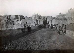 view Iran: a roadway leading towards a town with a decorative mosque (?); barefooted townspeople on the road. Photograph (by William Morgan Shuster ?), 1910/1920 (?).