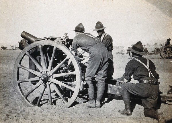 Moascar, Egypt: a New Zealand howitzer gun on a first world war camp with three soldiers. Photograph, 1914/1918 (?).