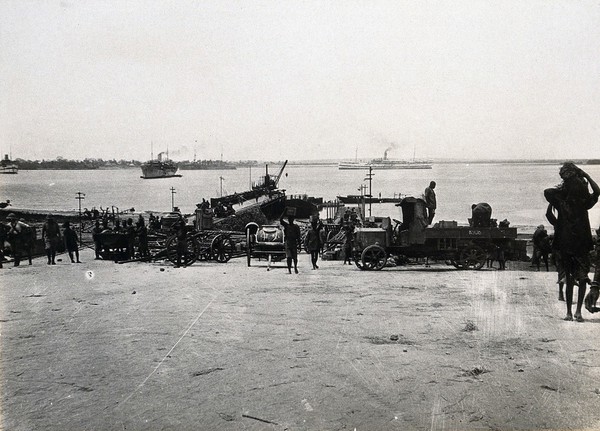 Kilwa Kisiwani, Tanzania: wharves with vehicles, soldiers and Tanzanians; boats in the background. Photograph, 1914/1918.