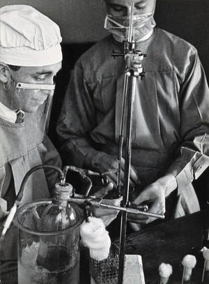 view Yellow fever: two scientists wearing face masks at work in a laboratory. Photograph, 1910/1930 (?).