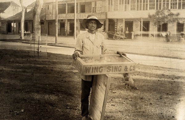 Port of Spain, Trinidad: a man selling cakes from a wooden glass-covered tray. Photograph, 1905/1915.