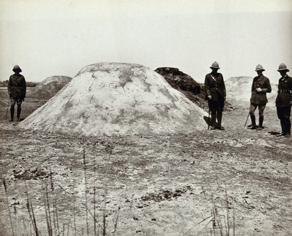 Mounds of horse-manure coated with sand and oil to prevent fly breeding, with Western (British?) men in military dress, Suez Canal Zone, Egypt (?). Photograph, ca. 1914.